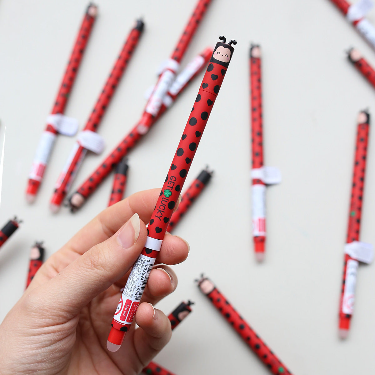 Hand holding a red and black ladybug-themed pen with more pens in the background.