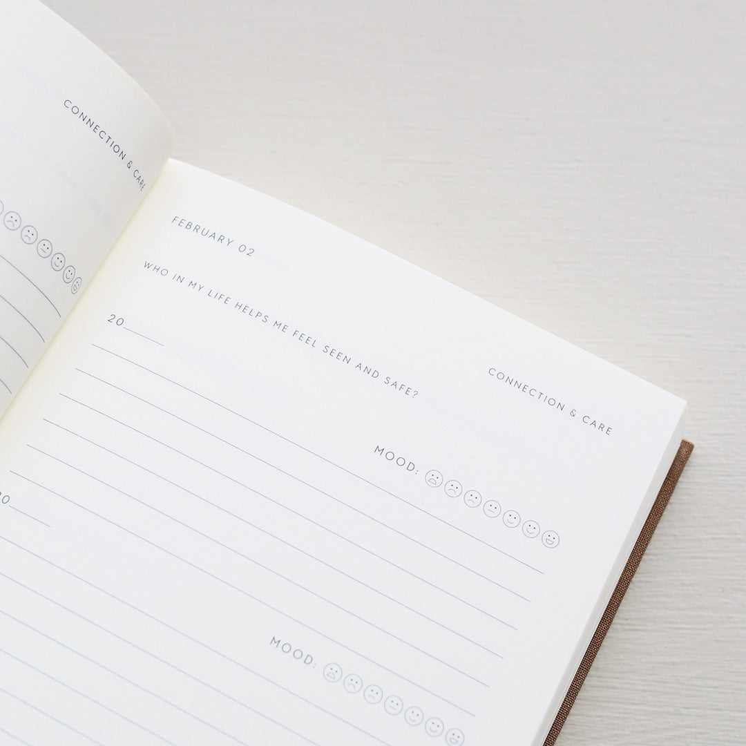 Open notebook with a page showing text prompts and emoji icons from 'Treårsdagbogen' on a light background