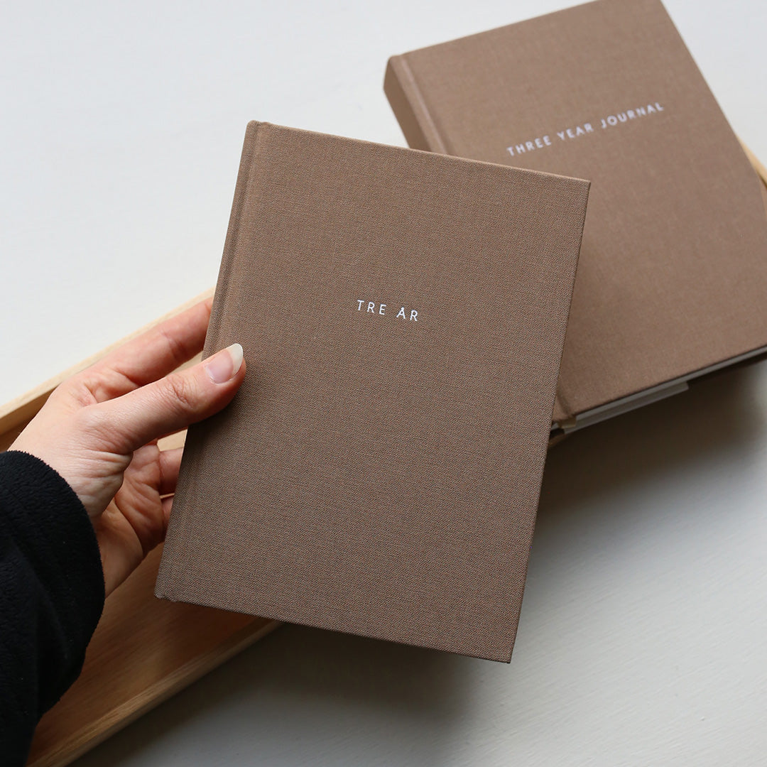 Brown journal with 'TRE ÅR' branding held by a hand on a light background