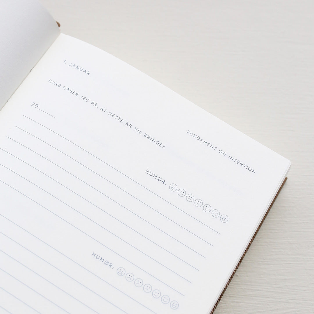 Open notebook with a page showing text and emoji icons from 'Treårsdagbogen' on a light background