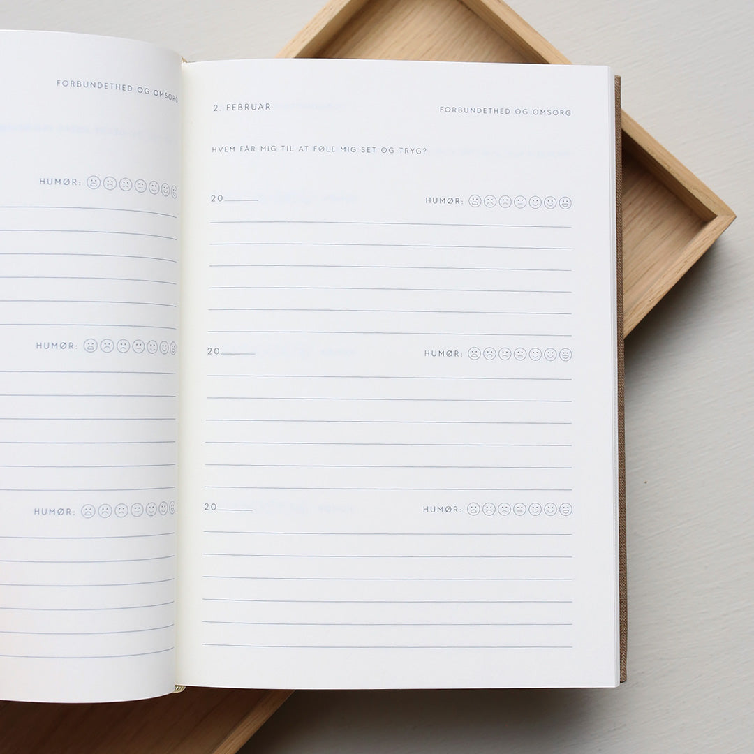 Open guided notebook with a page showing text and emoji icons from 'Treårsdagbogen' on a wooden tray