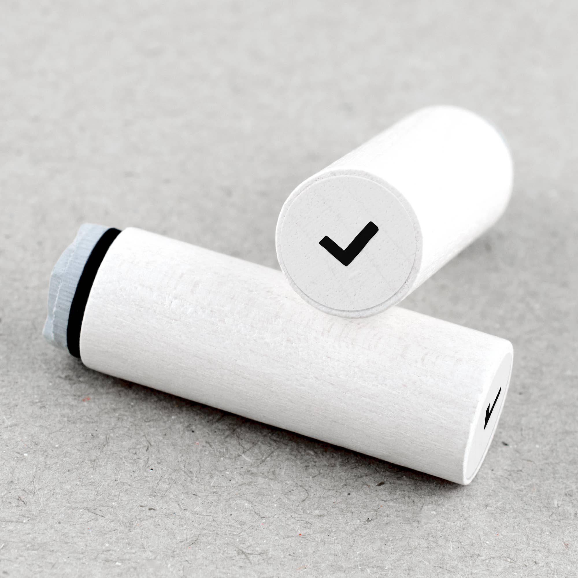 White wooden rubber stamps with a black band and check mark on a gray surface