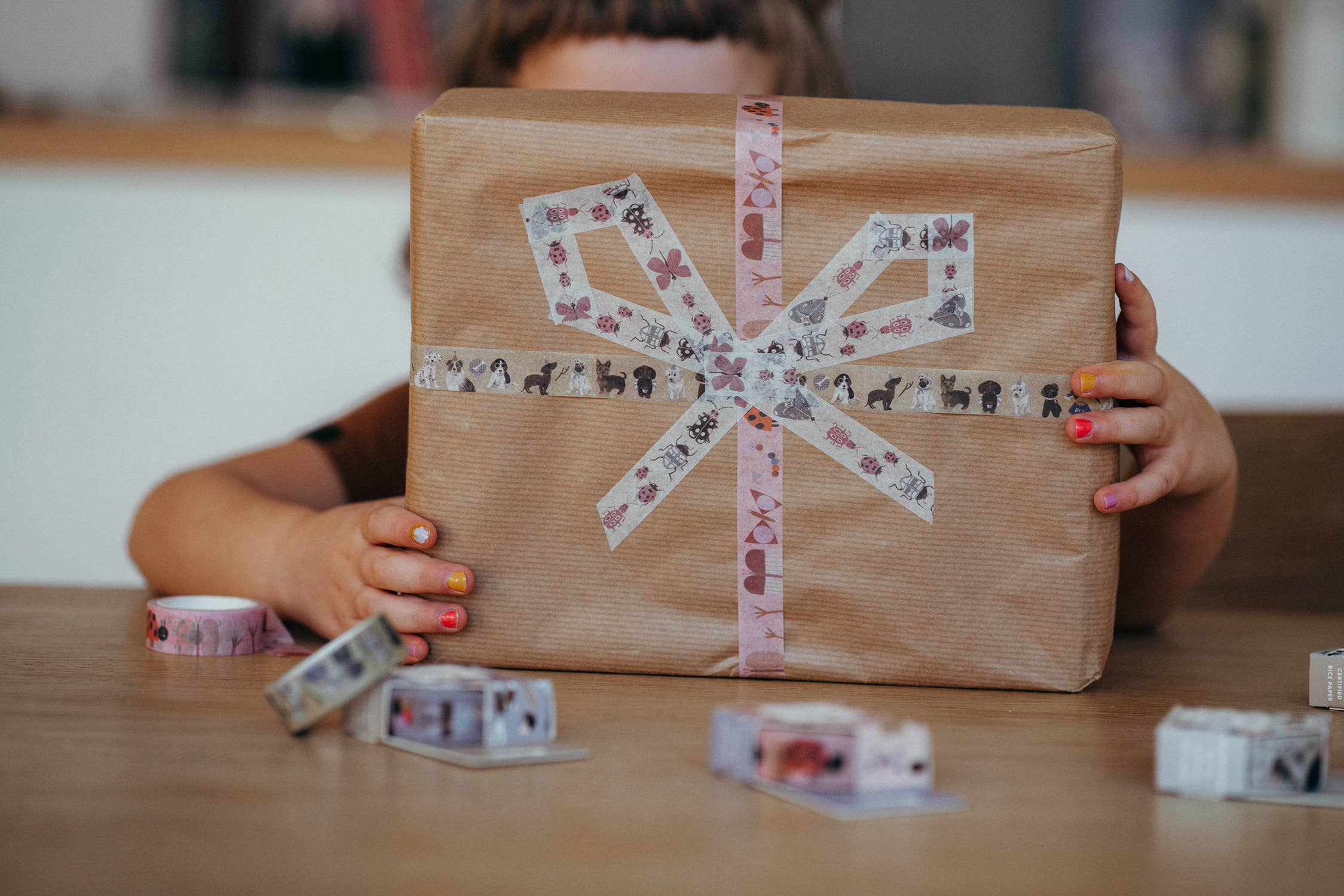 Person holding a wrapped gift with decorative tape, surrounded by additional tape rolls.