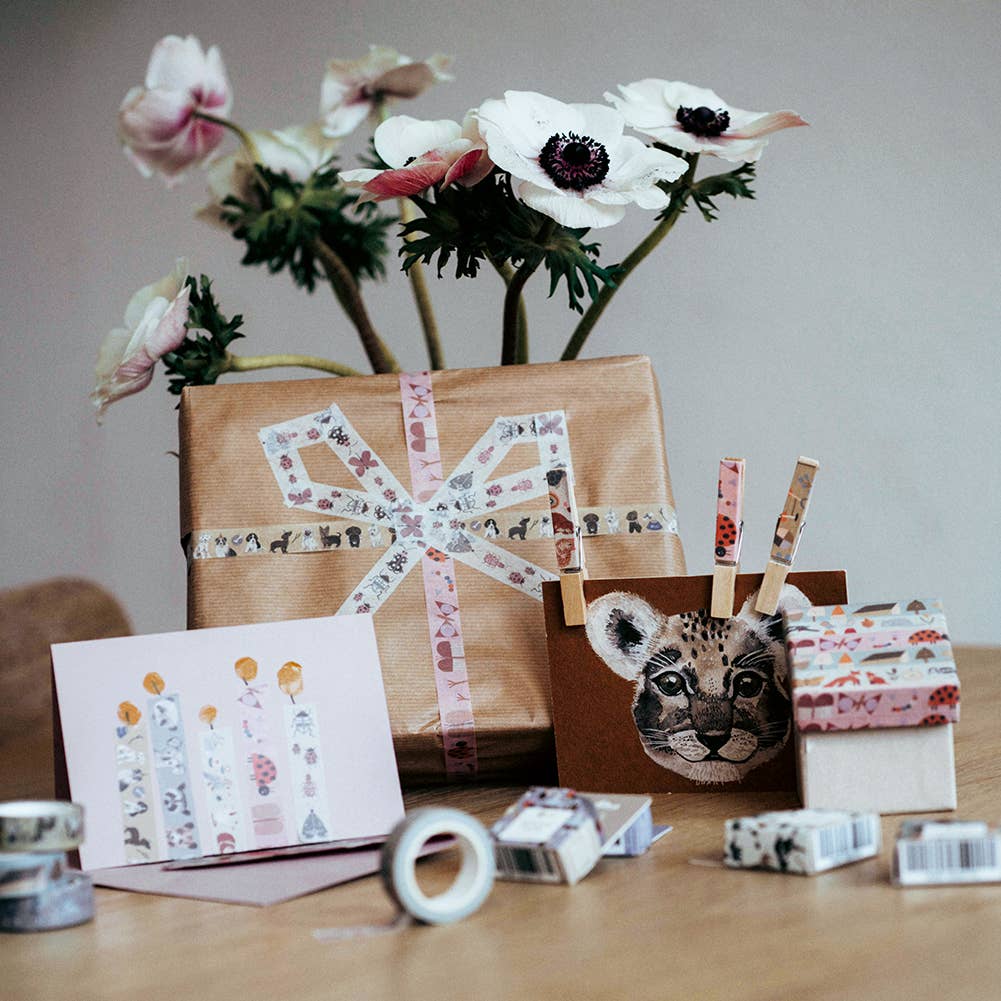 Gift wrapped in brown paper with decorative tape, flowers, and a card on a wooden surface.