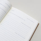 Open notebook with a page showing text and emoji icons from 'Treårsdagbogen' on a light background