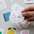 Hand holding a sticker with a bicycle design and 'Danmark' text on a surface with other stickers.
