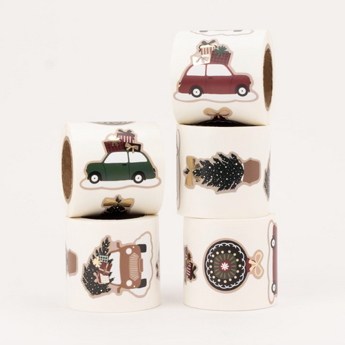 Four rolls of die-cut stickers stacked on a white background, featuring holiday illustrations including cars, Christmas trees, a vintage car, and a circular ornament design.