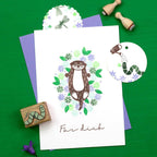 Card with an otter illustration otter and worm surrounded by flowers on a green background