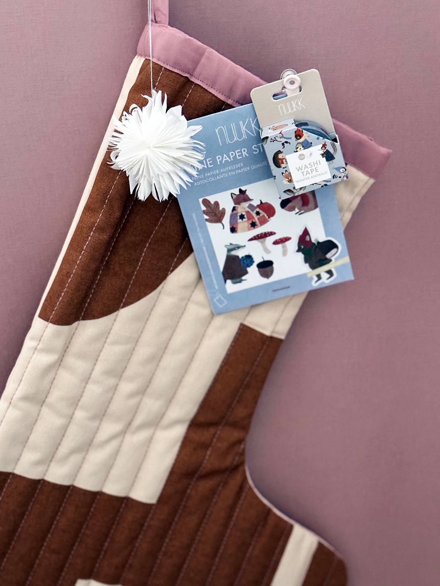 Quilted fabric with a flower, masking tape and a package of paper stickers on a pink background